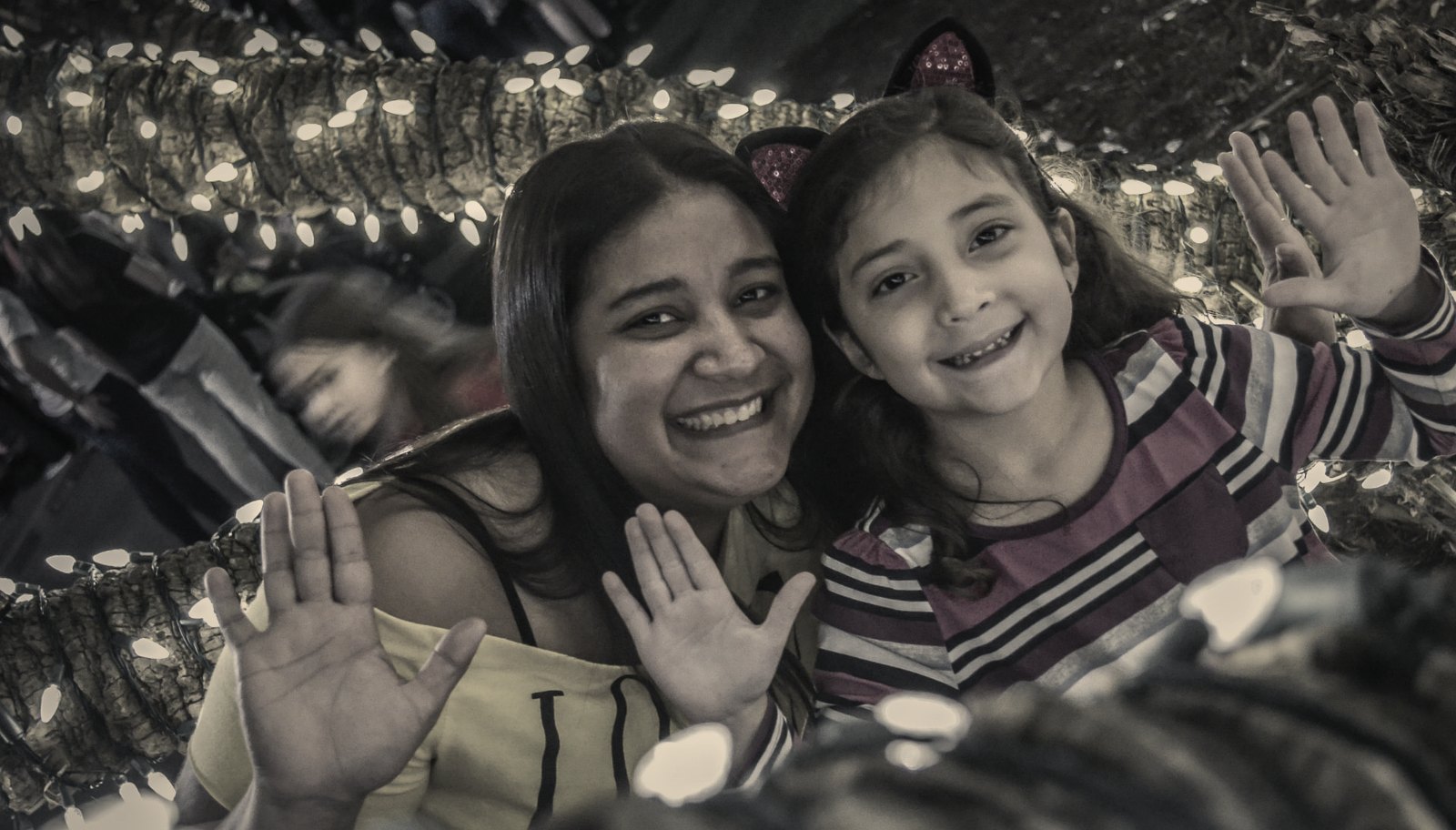 A mother and daughter smiling beneath strings of warm lights at an evening event