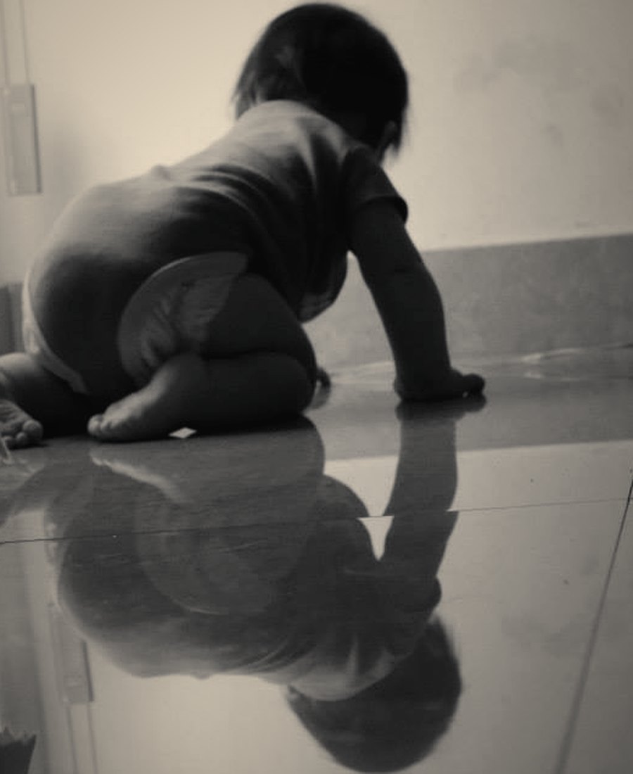 A crawling baby reflected on a polished floor, in black and white