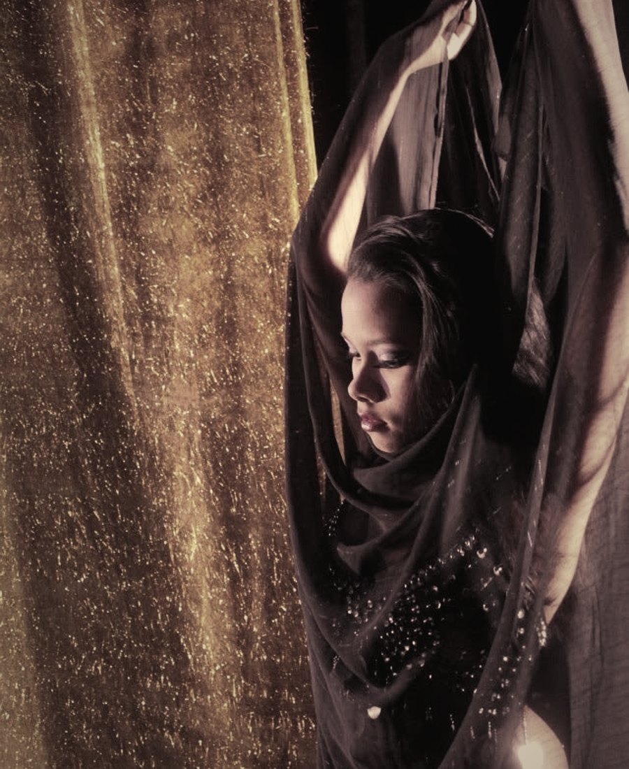 A dancer draped in flowing fabric before a shimmering golden curtain