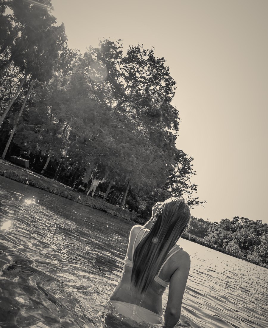 A woman standing in a sunlit lake, in black and white