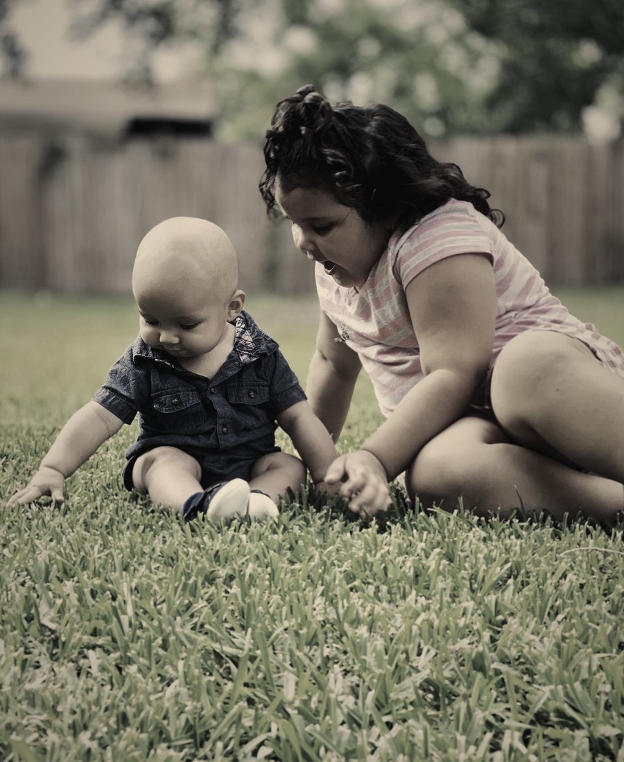 An older sister playing with her baby brother on the grass